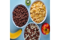 Bowls of breakfast cereals with chocolate loops, cornflakes, and mixed cocoa puffs beside fresh fruits